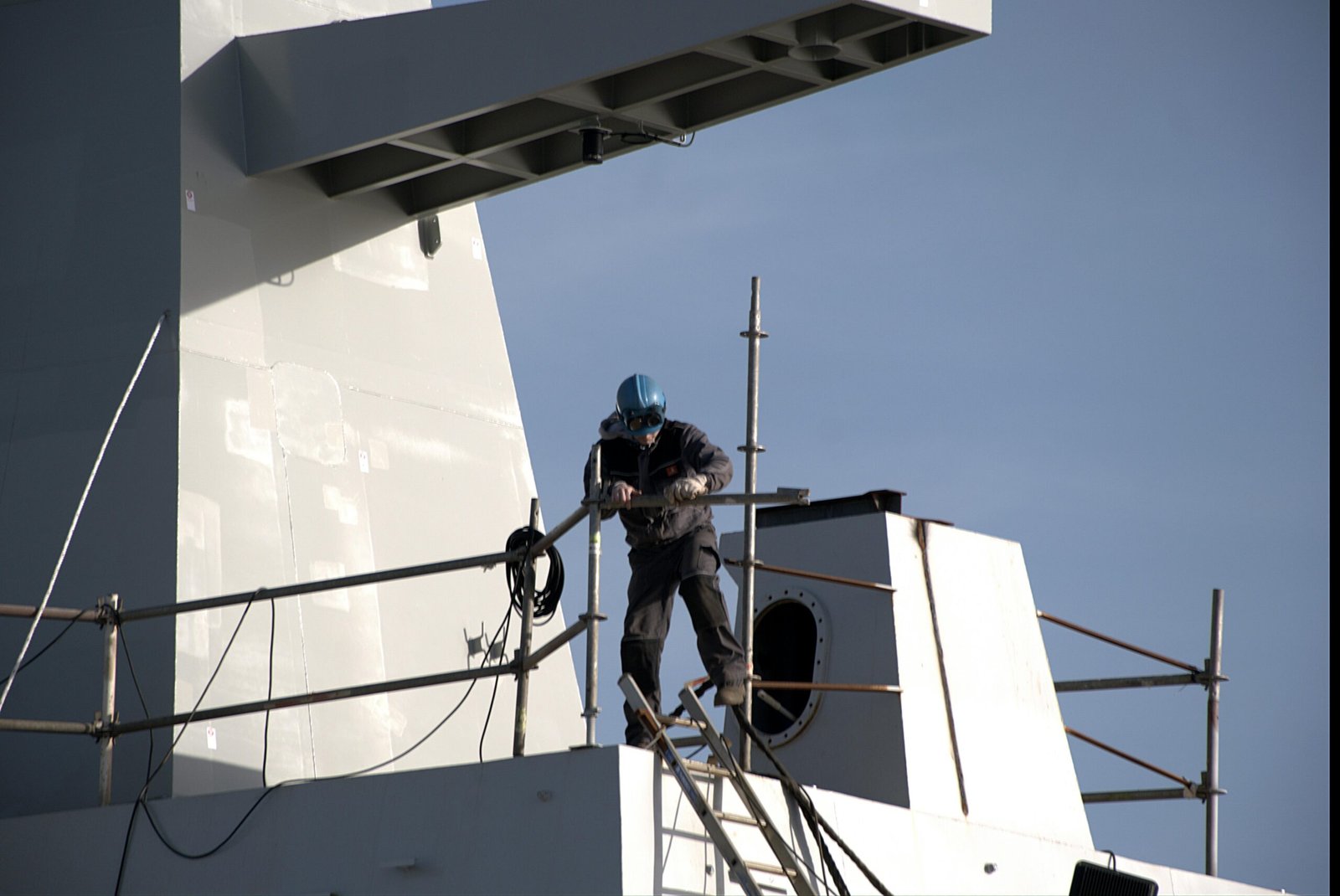 Lone industrial worker in safety gear securing a shipyard tower.